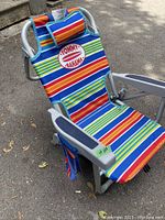 Front view of Tommy Bahama kids beach chair in bright multi-colored striped fabric with pillow and Tommy Bahama logo patch.