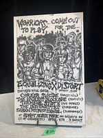 Photo of black and white wall art on board showing group of stylized characters, event text, and bands listed.