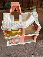 Front and angled left side view of the plastic Victorian dollhouse showing roof with decorative shingles and open interior space.