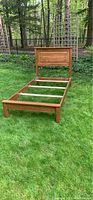 Full view of assembled oak twin bed frame including headboard, side rails, and footboard on grass outdoors showing the wood grain.