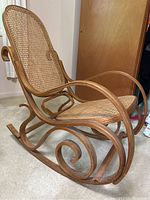 Side angle view of vintage bentwood cane rocking chair highlighting curved rockers and armrest details.