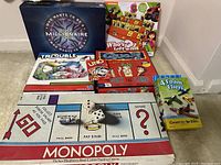 Photo showing Monopoly board game laid flat with pieces, WHO Wants to be a Millionaire, UNO cards, Quelf game box, Who's Left? game box, Trouble game box, and a foam airplane DIY kit.