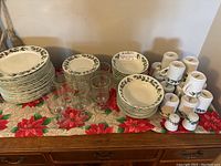 Full view of Christmas dishes including stacks of plates, bowls, glasses, and salt and pepper shakers arranged on festive poinsettia cloth
