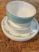 Stack of dishes showing dinner plates on bottom, lunch plates in middle, and bowls on top all with turquoise decorative borders.