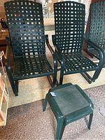 Front view of two dark green metal cantilever patio chairs with woven strap seats and backs, with square plastic table in front