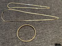 Two gold necklaces and one bangle bracelet laid on fabric background