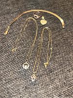 Overview of all items on dark textile background: collar necklace, three chains, heart pendant, ring.