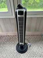 Full view of the Lasko tower fan standing on carpeted floor near window showing general condition and design.
