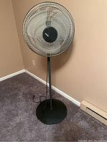 Front view of black Lasko oscillating pedestal fan showing mesh blade guard, white blades and black center hub with logo