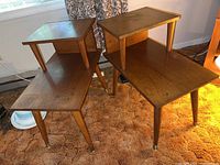 Front angle view of two brown wooden MCM step end tables, showing stepped top and tapered legs with brass caps