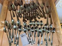 Drawer with assorted stainless steel spoons, forks, and serving utensils neatly arranged.