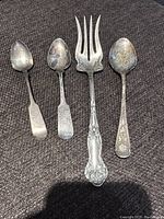 Four sterling silver flatware pieces (three spoons and one fork) shown laid out on a dark fabric.