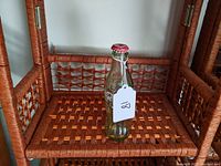 Full view of the clear glass Coca Cola bottle with red cap placed on a wicker shelf.