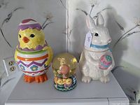Front view of all three items together: chick cookie jar, bunny cookie jar, and Easter snow globe