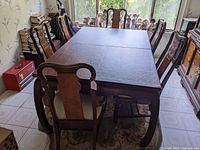 Photo showing full dining table with protective pad and six chairs around it in dining area with window light.