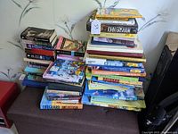 Large collection of books stacked on a piece of furniture showing a variety of genres and bindings