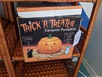 Box labeled Trick 'R Treater ceramic pumpkin with Halloween artwork and text stating it includes candle and is reusable after the season.