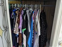 Clothing hanging on hangers inside a wardrobe, mostly women's tops and dresses with various colors and patterns including leopard print and floral designs.