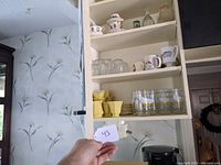 Kitchen cupboard shelf with glassware, mugs, and yellow dishware cups and bowls