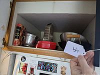 Wide view of shelf showing wok, grater, cookbook, ice bucket and a red container