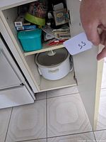 Open kitchen cupboard showing white crock pot with lid on bottom shelf.