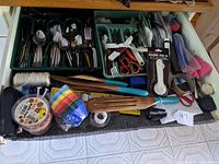 Full view of drawer showing flatware set, kitchen tools, wooden utensils, and various other small items organized in trays