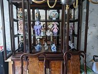 Front view of dining room hutch contents including multiple porcelain figurines and dolls arranged on shelves.