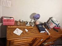 Top of wooden dresser holding various personal items including sunglasses, a lockbox, back scratcher, mirror, and organizer.