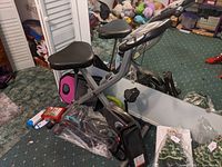 Side view of the Exerpeutic exercise bicycle showing adjustable seat, black plastic pedals, and parts of foot rest pedal and other items nearby.