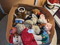 Large cardboard box filled with assorted dolls and plush stuffed animals, showing overview of contents.