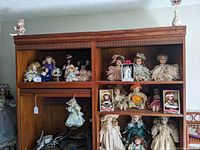 Wide shot of the entertainment wall units showing multiple porcelain dolls seated and standing in vintage style clothing including hats, lace, and ribbons.