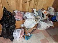 Photo of multiple large plastic bags and boxes against a wood-paneled wall containing assorted holiday decorations.