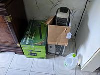 Overview photo of boxed leaf blower and tower-style space heater side by side on floor.