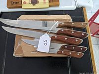 Five kitchen knives with wooden handles and metal rivets laid on a cardboard surface, showing blade edges and knife shapes