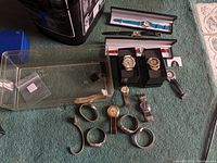Overview of all watches showing various styles, some in plastic boxes and others loose, mixed metal and leather bands