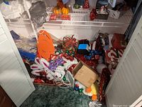 Wide view of closet floor showing various holiday decorations including orange pumpkin, red bows, tinsel garlands, and boxes