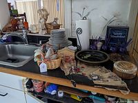 Photo of kitchen counter showing mixed lot of decorative fan, plates, glasses, carnival glass container, and other decor items