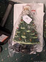 Ceramic Christmas tree with Santa top sealed in plastic packaging, showing a green tree with colorful bulbs and a Santa figure.