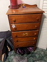 Front view of a small wooden dresser with five drawers and wooden knob handles, showing wear and tear.