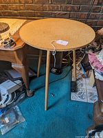 Full view of the small round table with three wooden screw-off legs attached and a particleboard top.