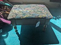 Front angle showing the footstool with floral tapestry upholstered top and wooden turned legs.