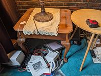 Full view of the walnut end/lamp table with a lace doily and lamp on top, showing carved table legs and matching furniture around it.
