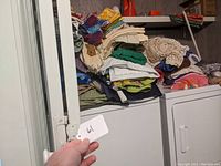 Stack of folded vintage towels and linens on top of a washing machine and dryer, showing various colors and textures including crocheted edges.