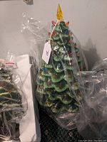 Full view of the ceramic Christmas tree wrapped in plastic, showing tree form, multiple colored 'lights', and star topper.