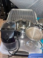 Photo showing La Pavoni electric coffee grinder, stainless steel saucepan with glass lid, metal broiler pan, insulated baking sheet, and Caribou Coffee pour-over set with glass carafe and metal filter on a tray.