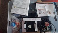 Photo showing AMD processor box with Certificate of Authenticity and various bottles of thermal paste and cleaning fluid, stock AMD fan visible in packaging.