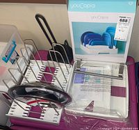 Photo showing YouCopia adjustable rack for pot lids and skillets with pot lids inserted, black paper towel holder, YouCopia container lid organizer in original box, and metal towel bar parts, illustrating condition and included items.