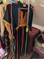 Front view of vintage Afghan embroidered dress with colorful vertical stripes and detailed embroidery around neckline and sleeves, hanging on clothing rack.