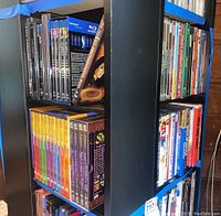 Photo of multiple DVDs and Blu-ray discs on black shelving unit, showing colorful DVD spines and boxed sets.