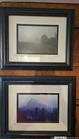 Framed black and white photographs by Amy Drake, showing two signed images titled 'Poor Farm Road' in black wood frames with white matting, one with foggy road, the other with barn and fence